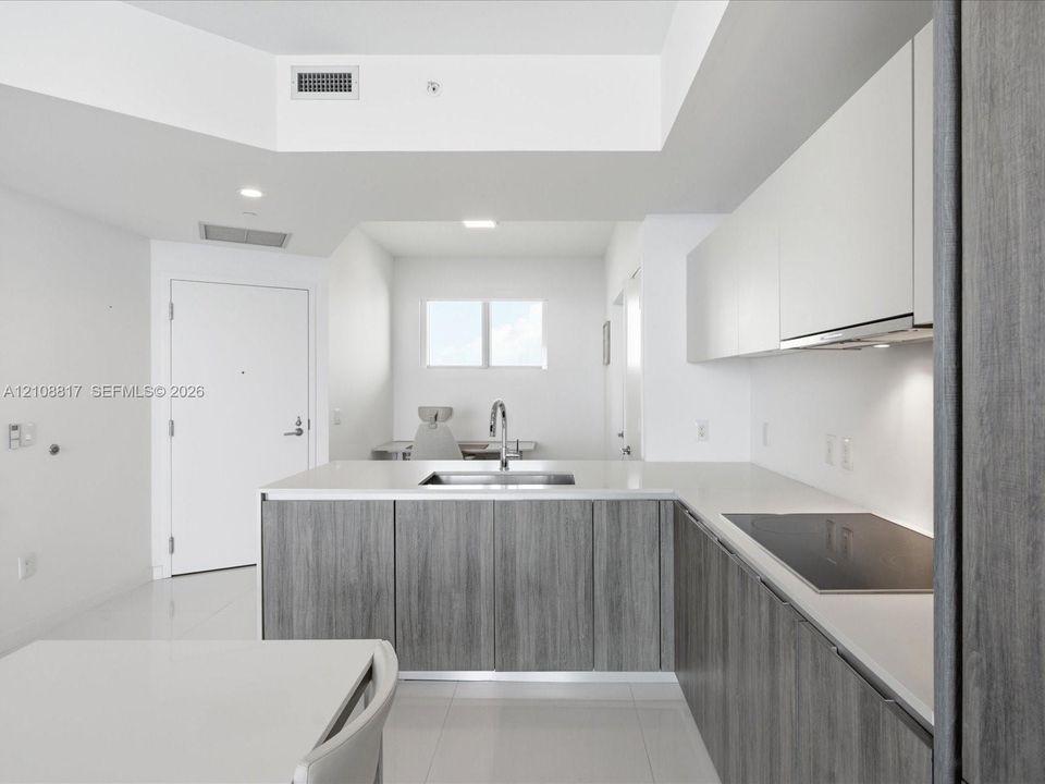 Modern kitchen featuring flat-panel cabinetry with wood-finish lower cupboards, solid surface countertops, an undermount sink with a gooseneck faucet, and an integrated induction cooktop