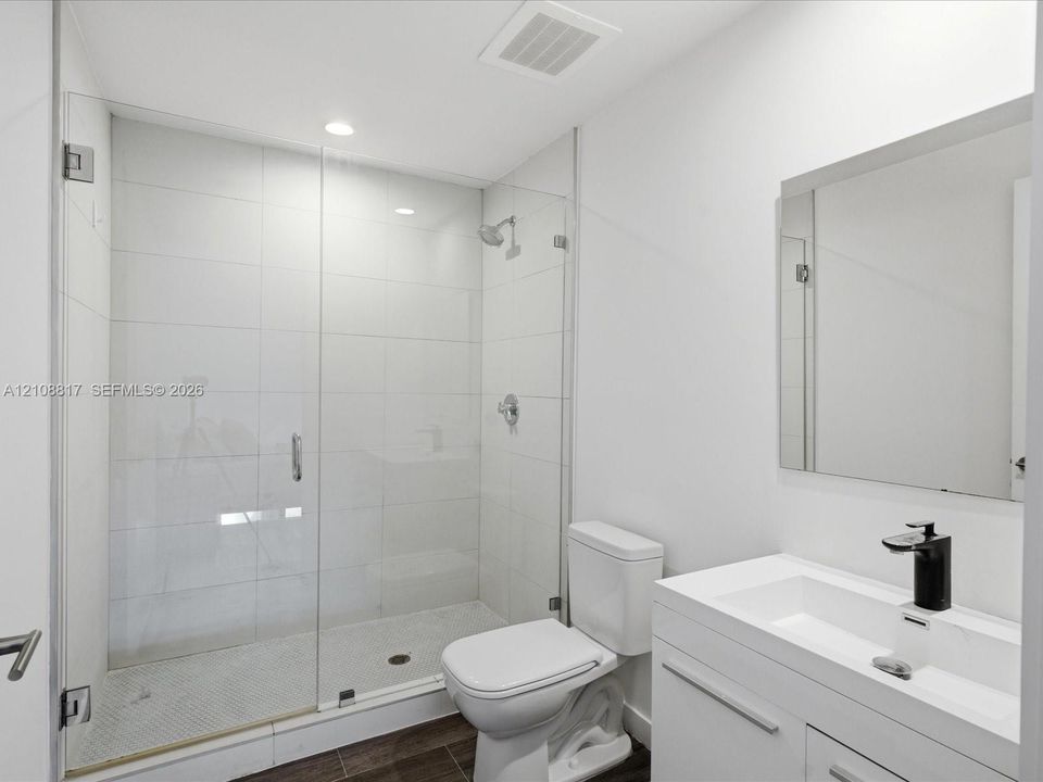 Walk-in shower with a glass enclosure, floor-to-ceiling white tile, modern vanity with a rectangular sink, matte black faucet, and polished mirror