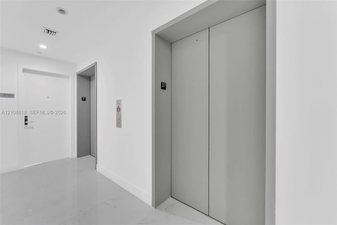Hallway featuring dual elevator access, sleek white walls, high-gloss tile flooring, and flush-mount recessed lighting