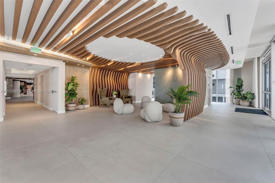 Expansive lobby featuring large-format tile flooring, a custom wood-slat ceiling installation with curved architectural detailing, and recessed lighting