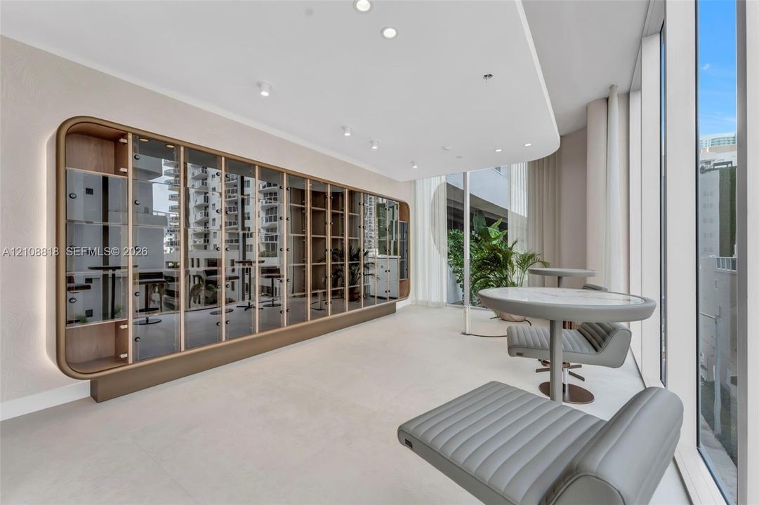 Built-in floor-to-ceiling display cabinetry with rounded corners, integrated backlighting, glass shelving, and full-height windows with light-toned flooring and recessed ceiling lighting