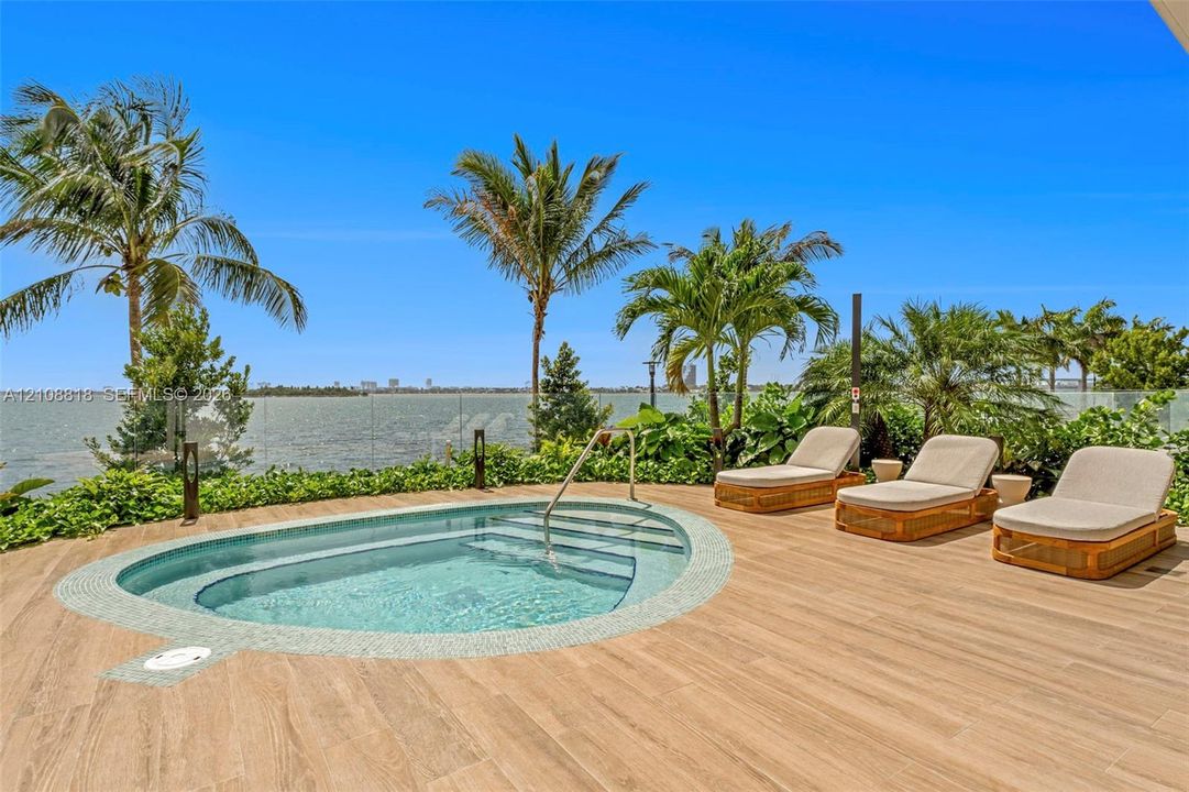 In-ground spa with tile surround, wood-finish decking, glass panel railing, and mature palm trees