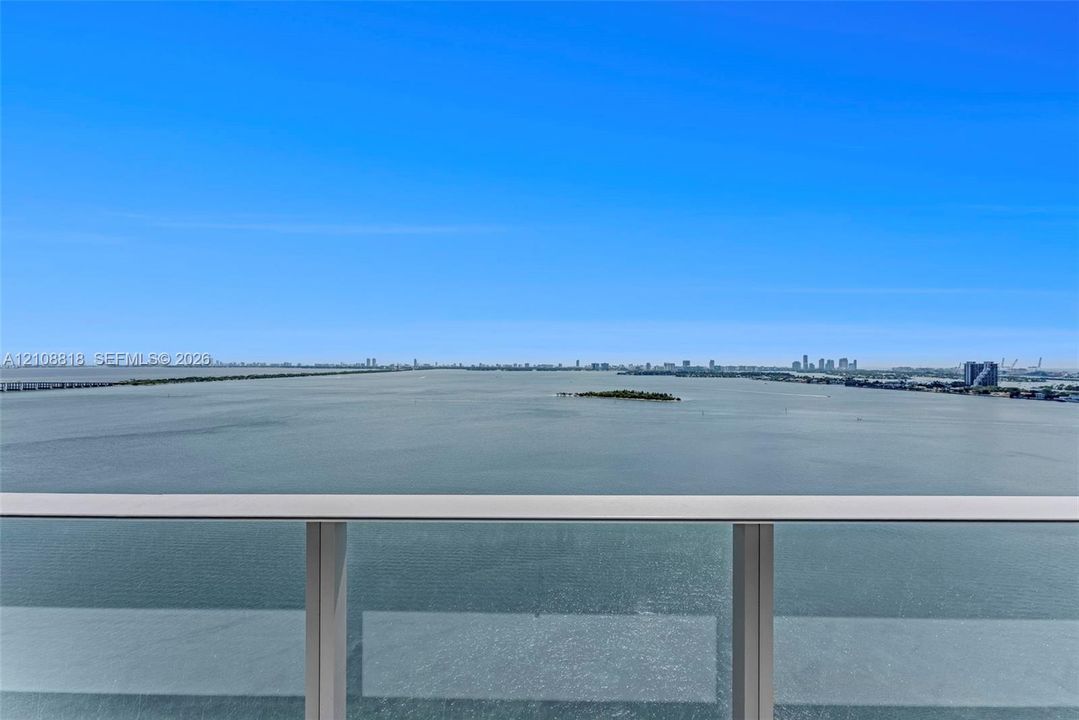 Open-air balcony featuring a glass and metal railing system with expansive water and distant skyline scenery