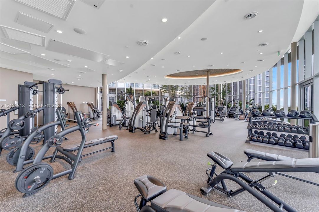 Fitness center featuring a curved ceiling with recessed lighting, floor-to-ceiling windows, and resilient athletic flooring