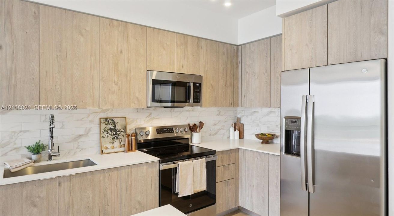 Kitchen featuring light wood-finish cabinetry, solid surface countertops, stainless steel appliances, and a horizontal tile backsplash