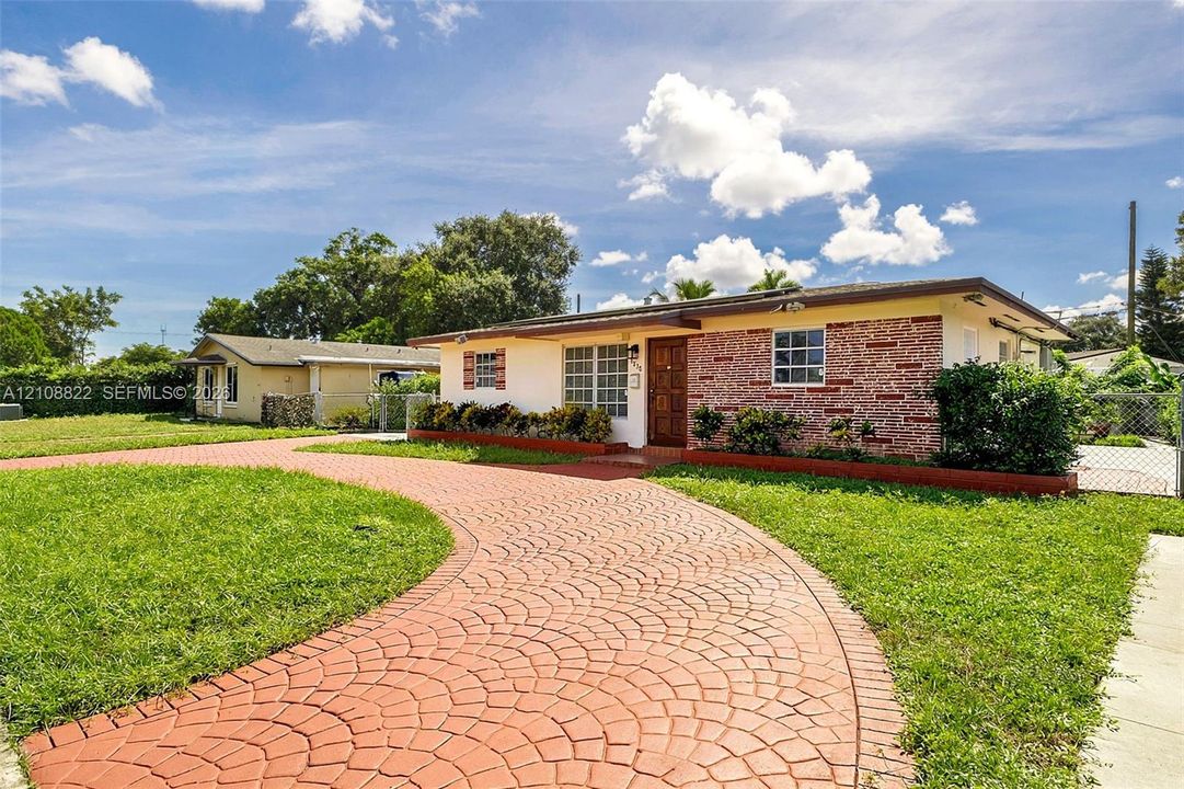 Exterior facade featuring a brick accent wall, a circular patterned paver driveway, and a grid-pane window configuration
