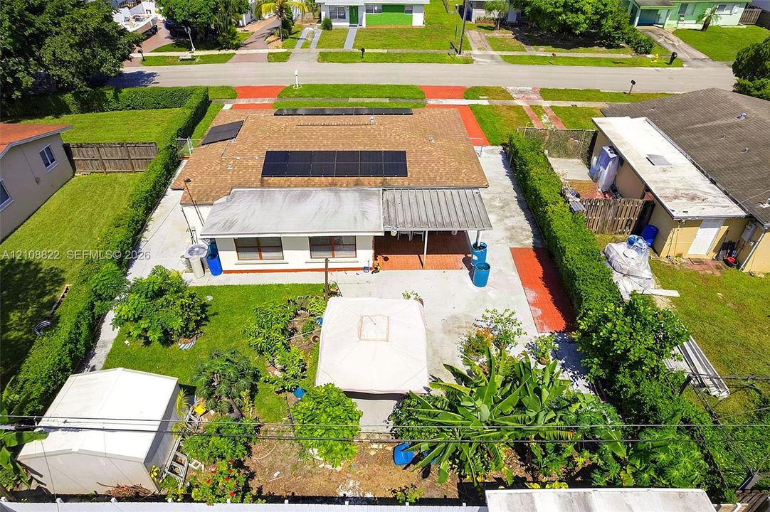Exterior featuring a shingle roof equipped with solar panels, a covered patio, a concrete rear yard, and mature perimeter hedging