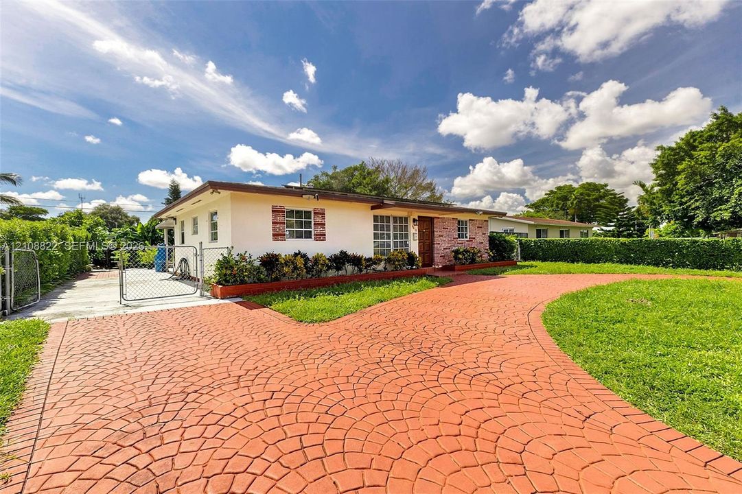 Single-story exterior featuring a decorative stamped concrete driveway, exterior brick masonry accents, low-maintenance landscaping, and a chain-link fenced perimeter