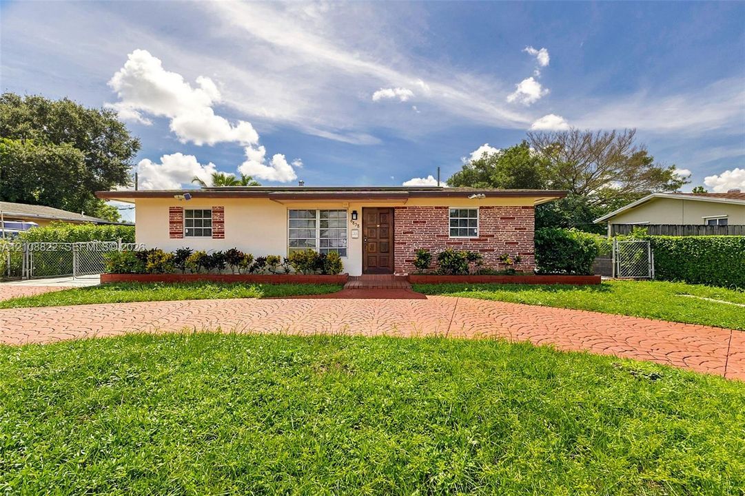 Single-story exterior featuring a brick facade, stucco siding, a patterned concrete driveway, and exterior shutter accents