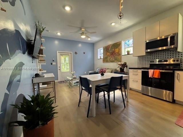Open-concept layout featuring wood-finish flooring, recessed lighting, white cabinetry, a black-and-white patterned backsplash, and stainless steel kitchen appliances