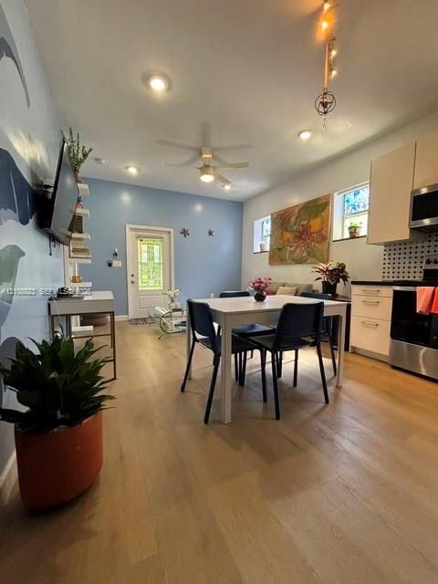 Open-concept interior featuring light wood-finish flooring, recessed lighting, ceiling fan, and white cabinetry with a high-contrast decorative backsplash