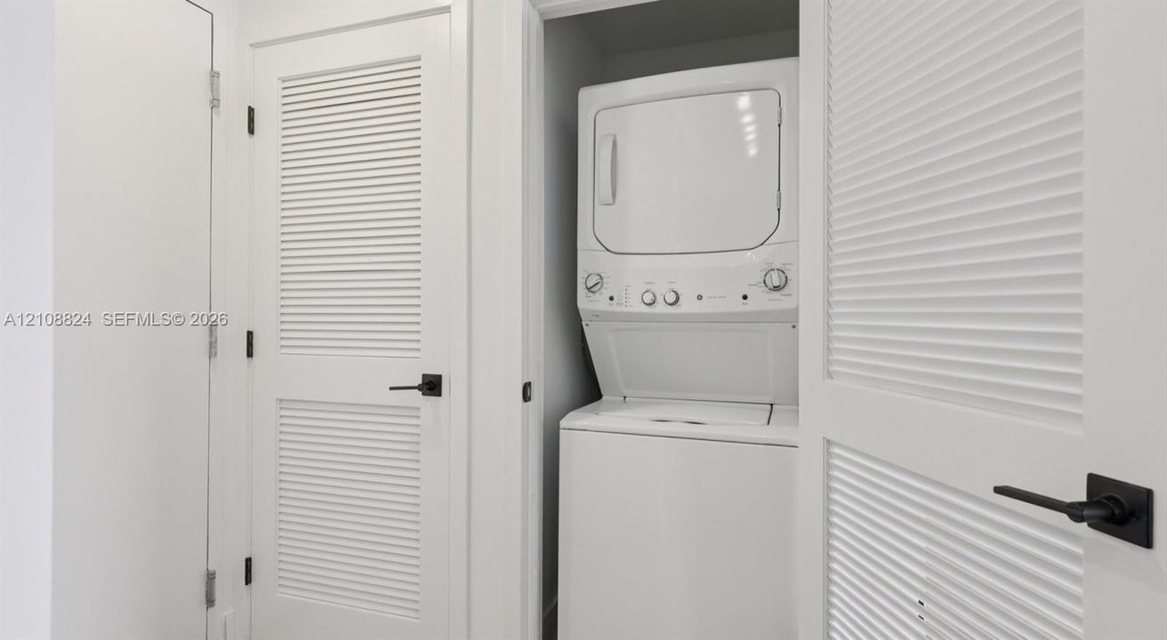 Laundry closet featuring a stackable washer and dryer unit, white louvered doors, and matte black hardware