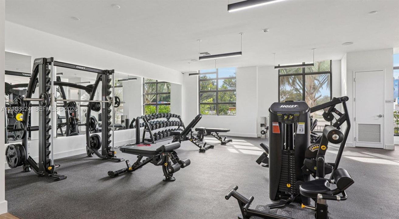 Fitness center featuring rubber flooring, floor-to-ceiling mirrors, industrial-style track lighting, and multi-pane windows