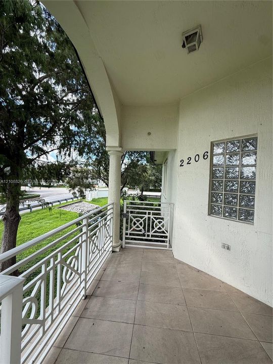 Covered balcony featuring tile flooring, decorative metal railing, a structural column, and a glass block window