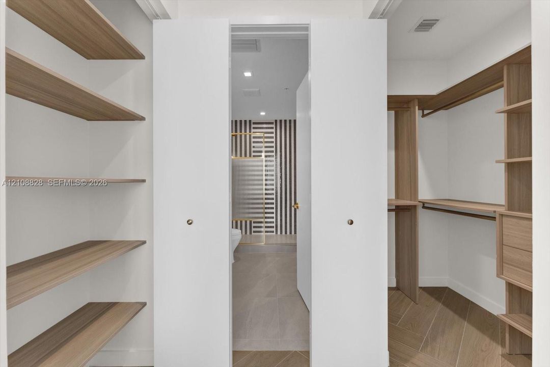 Walk-in closet featuring custom wood-finish built-in shelving, integrated hanging rods, and wood-finish flooring in a herringbone pattern
