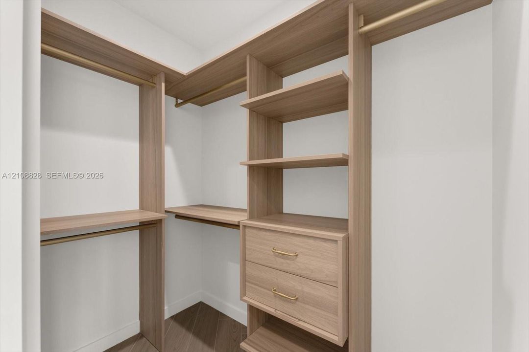 Walk-in closet featuring custom wood-finish shelving, integrated drawers, metal hanging rods, and wood-finish flooring