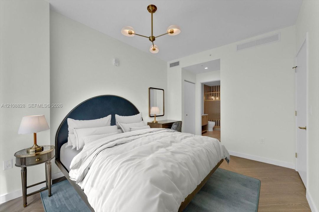 Modern bedroom featuring wood-finish flooring, a multi-arm brass finish chandelier, and neutral wall color