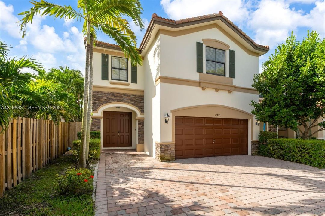 Two-story exterior featuring a stone veneer facade, stucco finish, arched entryway, double wood-panel doors, and a paver driveway