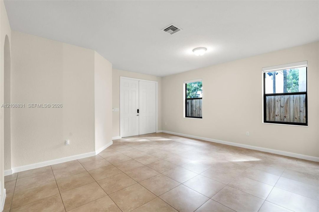 Neutral-toned interior space featuring light-colored tile flooring, double-door entry, and multiple windows with dark frames