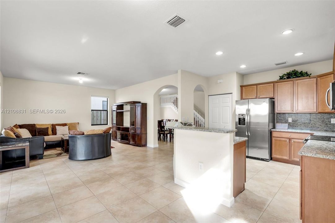 Open-concept living space featuring ceramic tile flooring, kitchen island with stone countertop, stainless steel refrigerator, recessed lighting, and arched architectural details