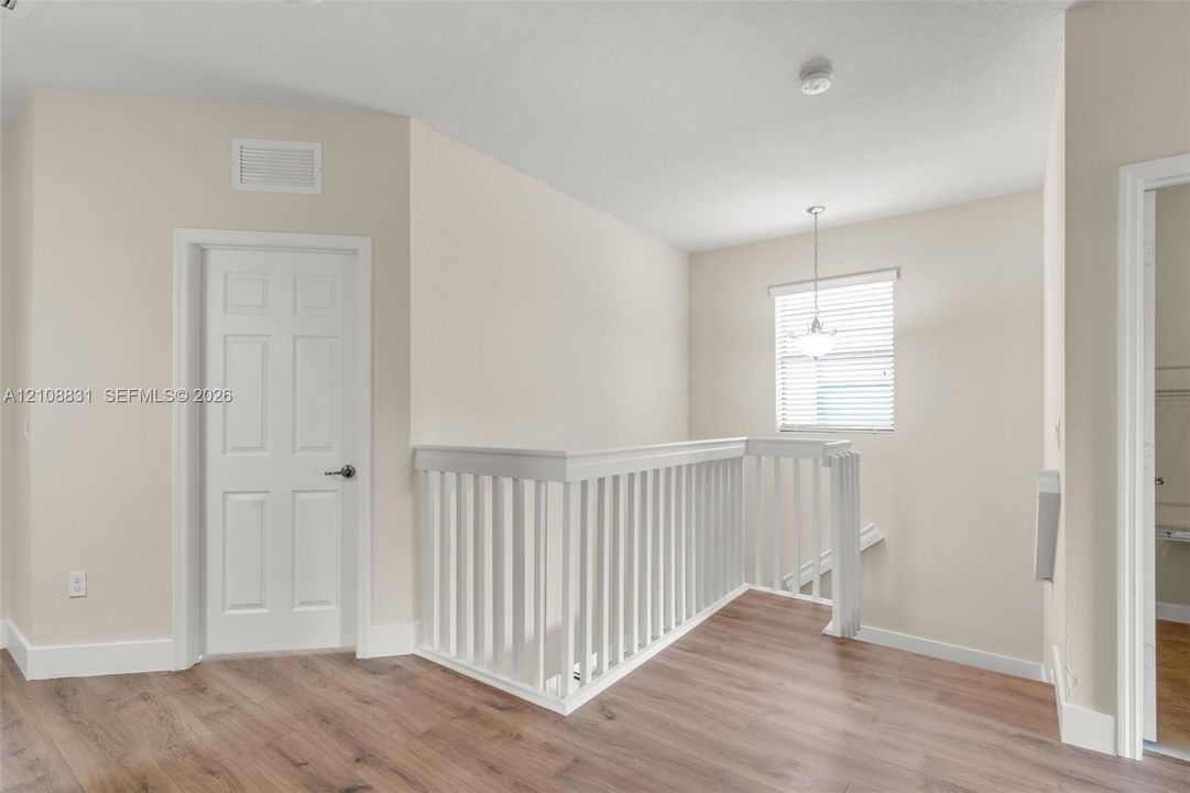 Wood-finish flooring, white spindle balustrade, neutral wall tones, multi-panel interior door, and pendant lighting