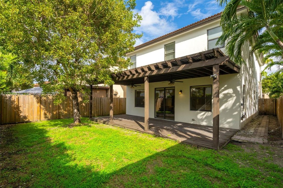 Rear exterior featuring a wood-decked patio with a pergola, stucco facade, manicured lawn, and wood privacy fencing