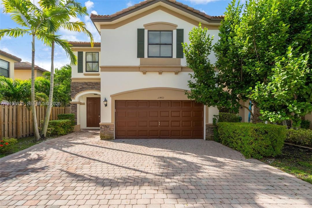 Two-story exterior featuring a paver driveway, stone veneer accents, integrated two-car garage, and decorative shutters