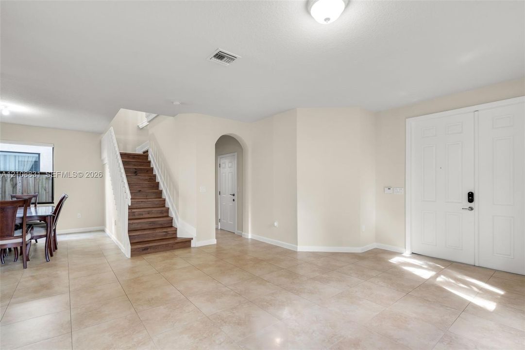 Foyer area featuring large-format ceramic tile flooring, a staircase with wood-finish treads and a white balustrade, arched architectural detailing, and a multi-panel double entry door