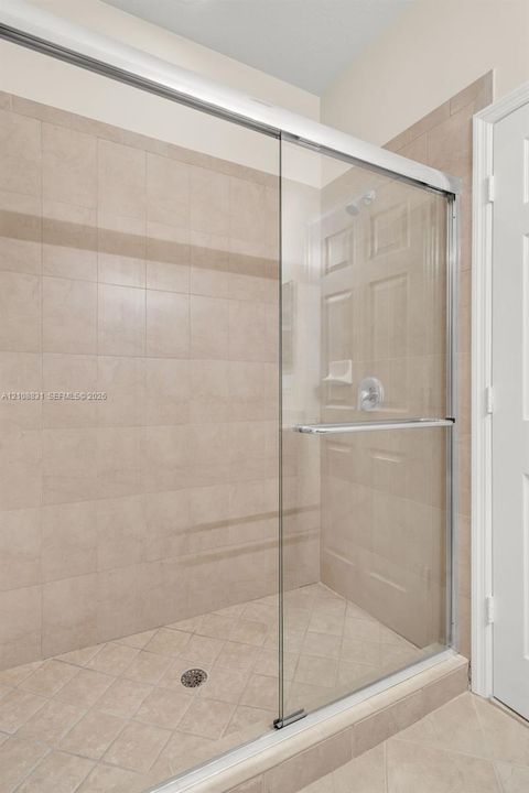 Walk-in shower featuring glass sliding doors, neutral ceramic tile surround, integrated soap niche, and polished chrome hardware