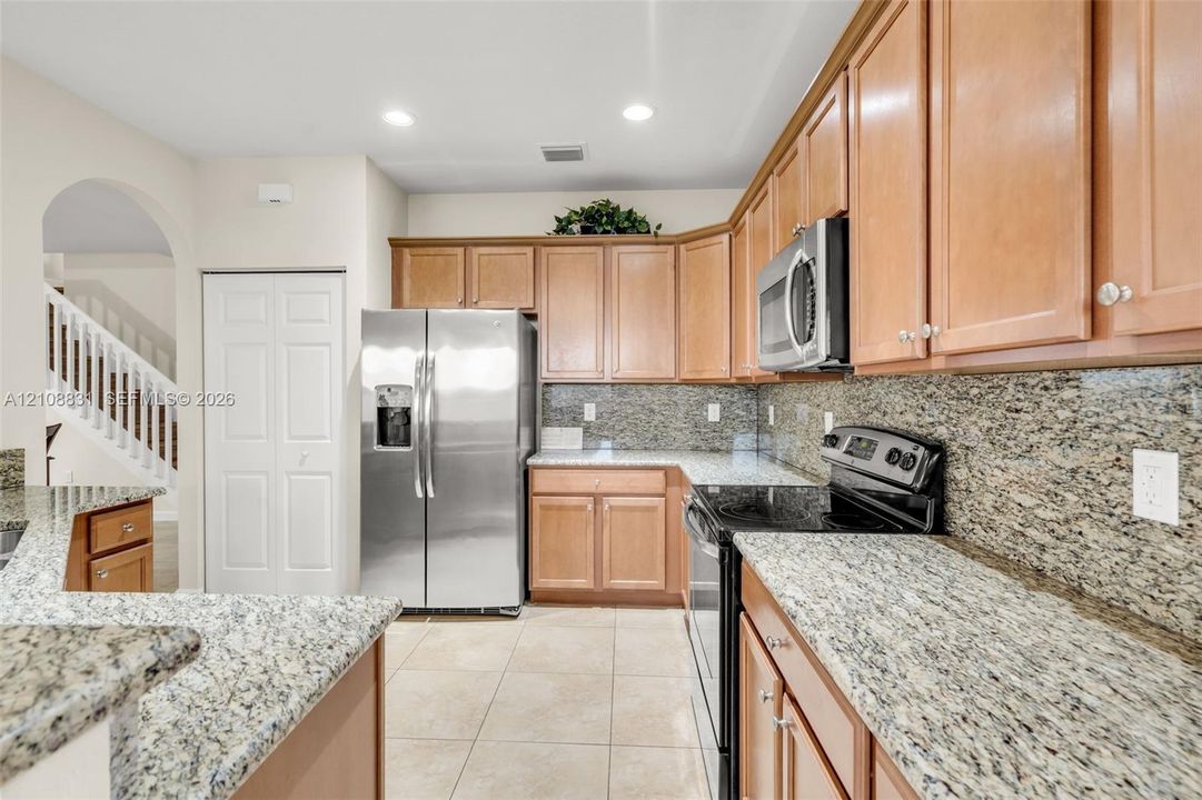 Kitchen featuring wood cabinetry, stone countertops, stone tile backsplash, stainless steel refrigerator, and built-in microwave