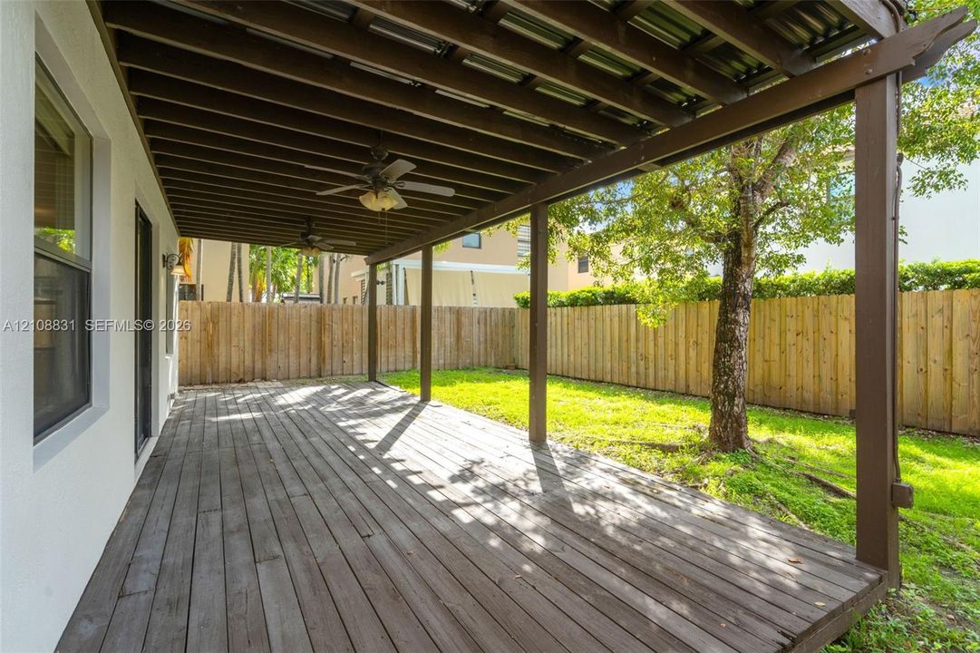 Covered wooden deck featuring an overhead trellis structure with mounted ceiling fans, enclosed by a full-height perimeter wood fence