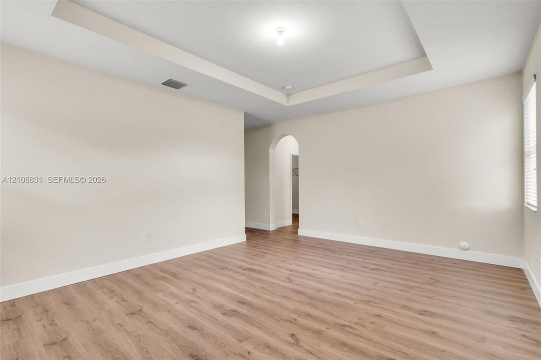 Interior space featuring tray ceilings, wood-finish flooring, neutral wall paint, and an arched entryway