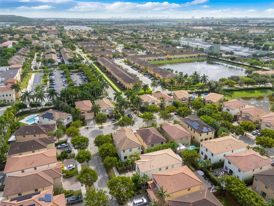 Aerial perspective of a planned community featuring multi-story residences with tiled roofs, established landscaping, interspersed palm trees, and a central water feature
