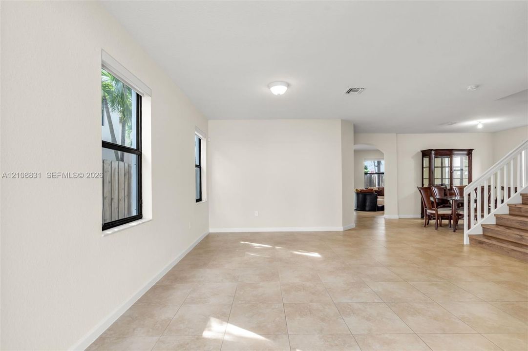 Open interior space featuring light-toned tile flooring, neutral wall finishes, recessed lighting, and a staircase with white balusters and wood-finish treads