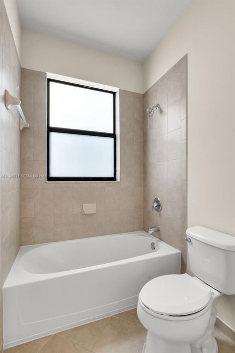 Bathtub with shower combination featuring neutral-toned tile surround, polished metal fixtures, and a single-hung window