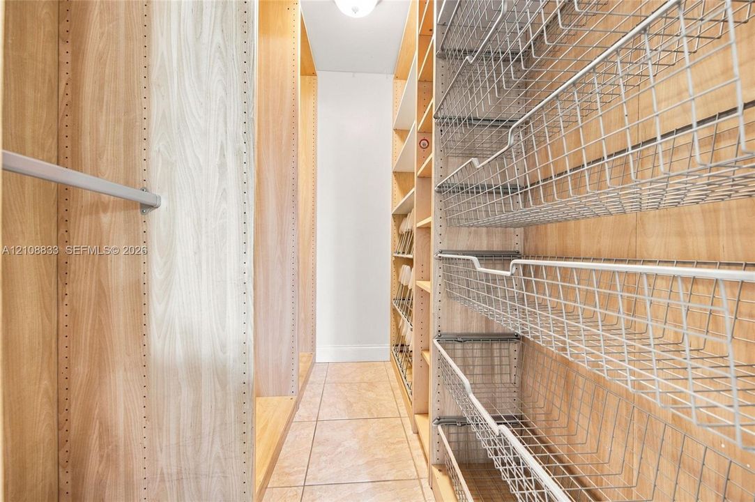 Custom storage system featuring light wood-finish shelving, integrated metal pull-out wire baskets, adjustable hanging rods, and tile flooring