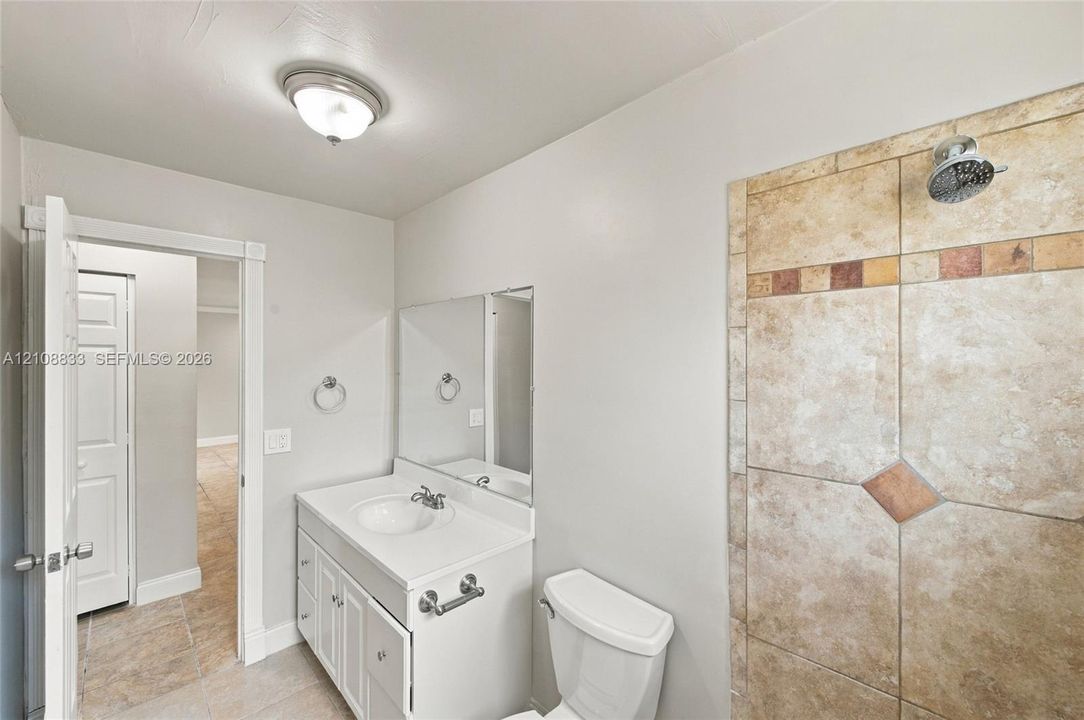 Bathroom featuring white cabinetry, integrated sink, wall-mounted mirror, and tile-surround shower with decorative stone-finish accents