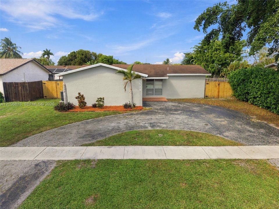 Single-story residence featuring a low-slope roof, textured exterior finish, circular paved driveway, and wood-panel fencing