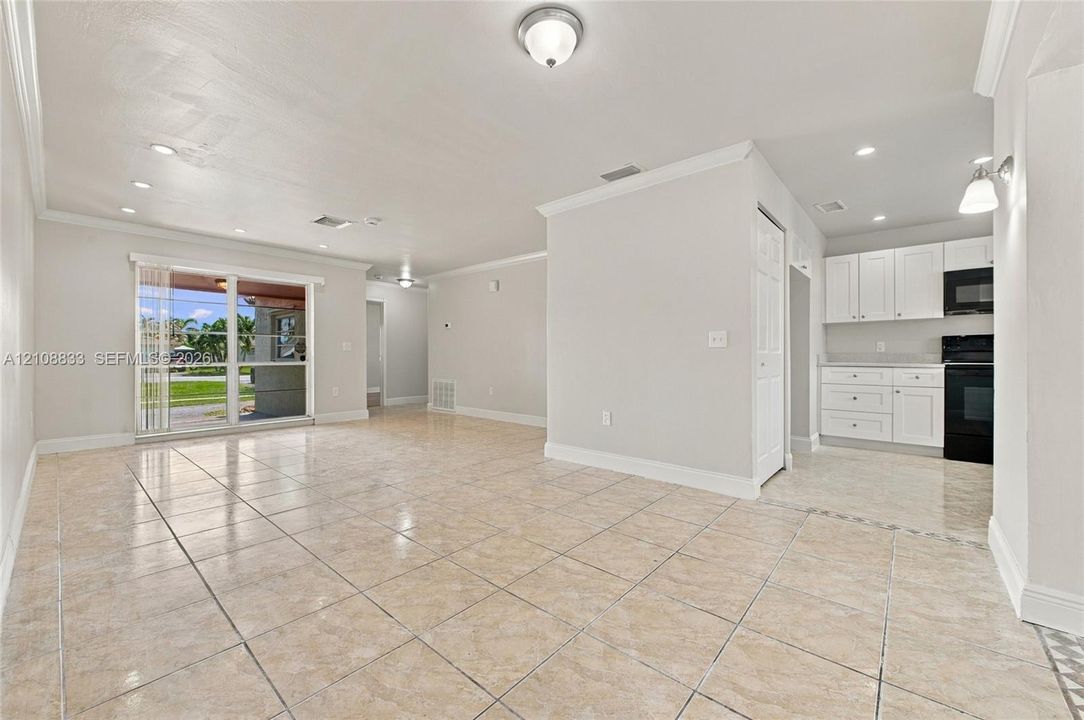 Open interior featuring neutral tile flooring, crown molding, recessed lighting, and a kitchen equipped with white cabinetry and built-in appliances