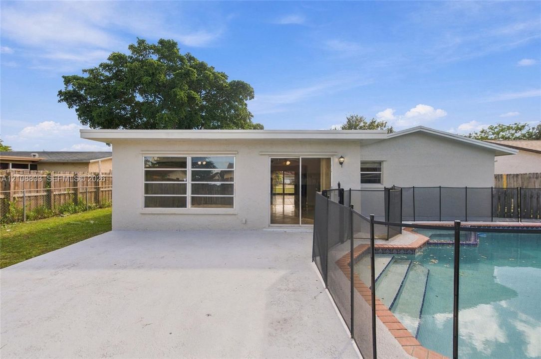 Rear exterior featuring a concrete patio, a swimming pool with tiered steps, an integrated safety fence, and a wood-slat perimeter fence