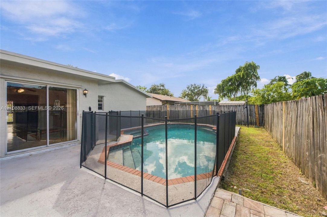 Backyard featuring an in-ground swimming pool with brick coping, a protective mesh safety fence, a concrete patio, and a wood privacy fence