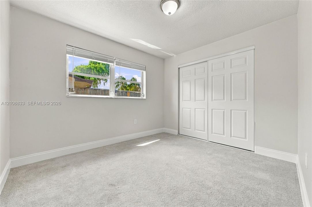 Neutral-toned carpeting, white six-panel closet doors, ceiling-mounted lighting, and a window with horizontal blinds