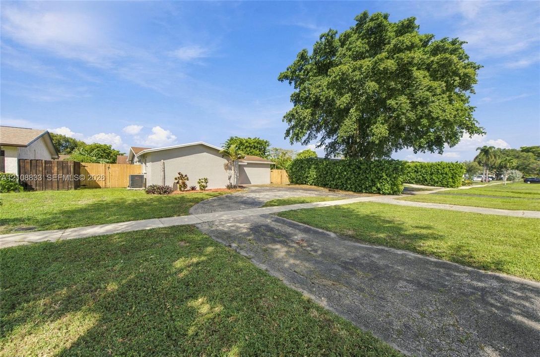 Exterior featuring a concrete driveway, mature landscaping, and a wood privacy fence