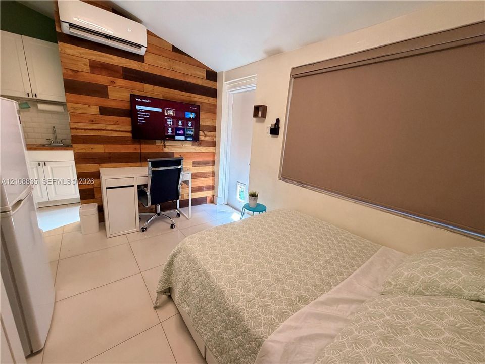 Vaulted ceiling with a wall-mounted ductless mini-split system, accent wall featuring horizontal wood planking, and large-format tile flooring