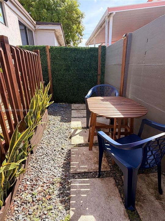 Private outdoor area featuring a stone paver path, gravel ground cover, stained wood-slat fencing, and a vertical faux-foliage privacy screen