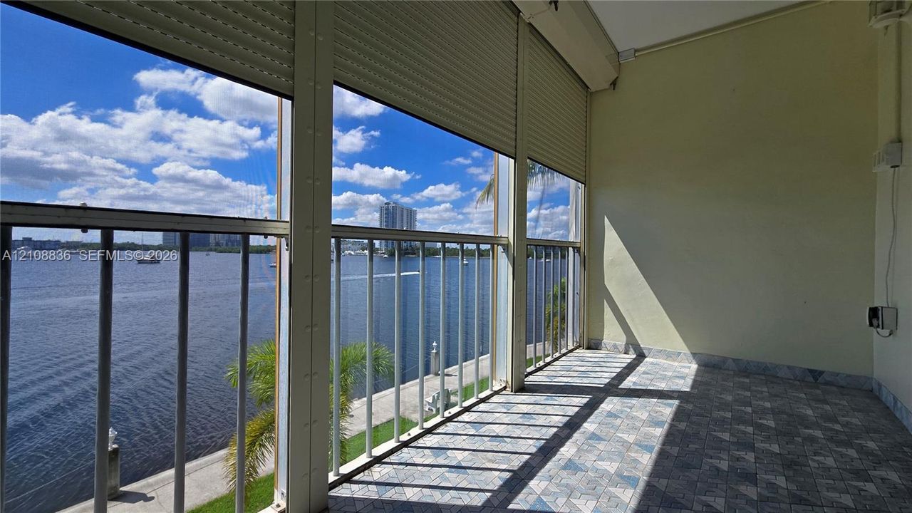 Enclosed balcony featuring patterned tile flooring, metal railings, and retractable exterior security shutters