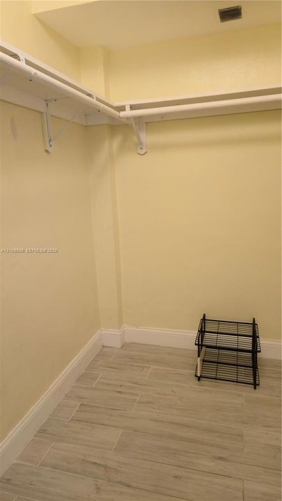 Walk-in storage area featuring wood-finish tile flooring and wraparound white shelving