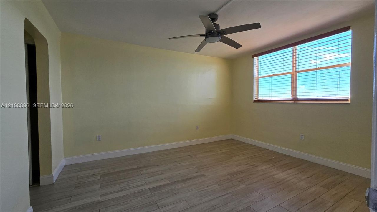 Interior room featuring wood-finish tile flooring, a neutral-toned wall finish, a multi-blade ceiling fan, and a large horizontal window with slatted blinds
