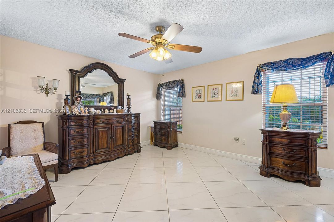 Large-format neutral tile flooring, ceiling fan with integrated light fixture, dual wall-mounted light sconces, and double-pane windows with horizontal blinds