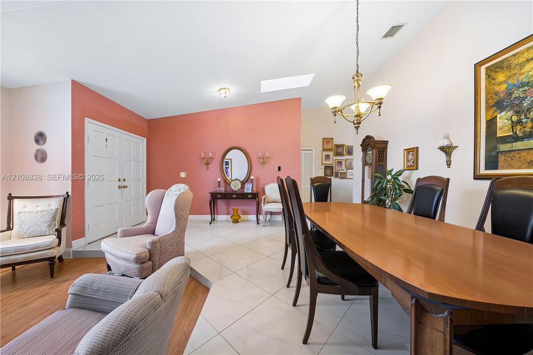 Open-concept area featuring vaulted ceilings, oversized tile flooring, wood-finish flooring, a skylight, and a decorative chandelier